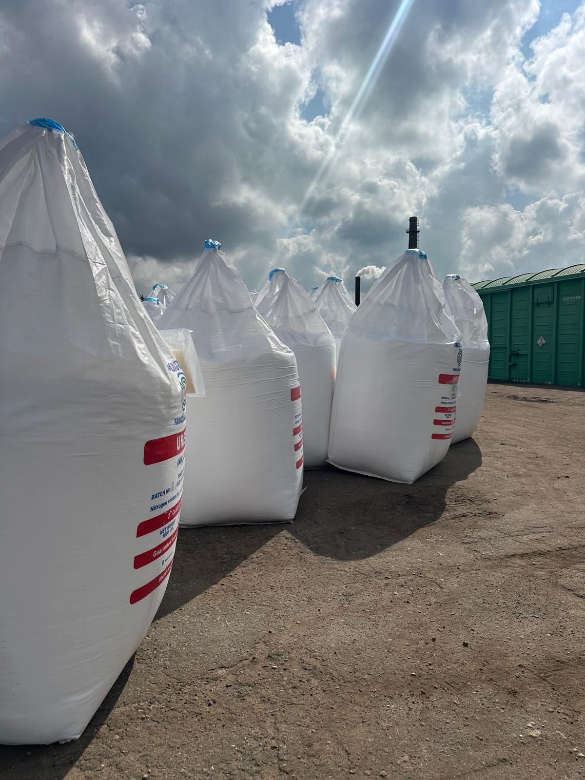 Rows of white Urea big bags in an open yard under a dramatic cloudy sky